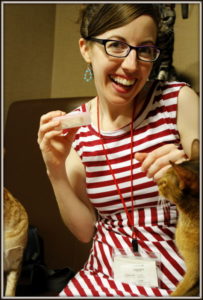 A woman in a red and white striped dress petting a kitten smiles at the camera.