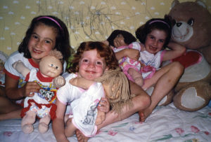 Three young girls lay in bed with matching cabbage pach dolls and nightgowns.