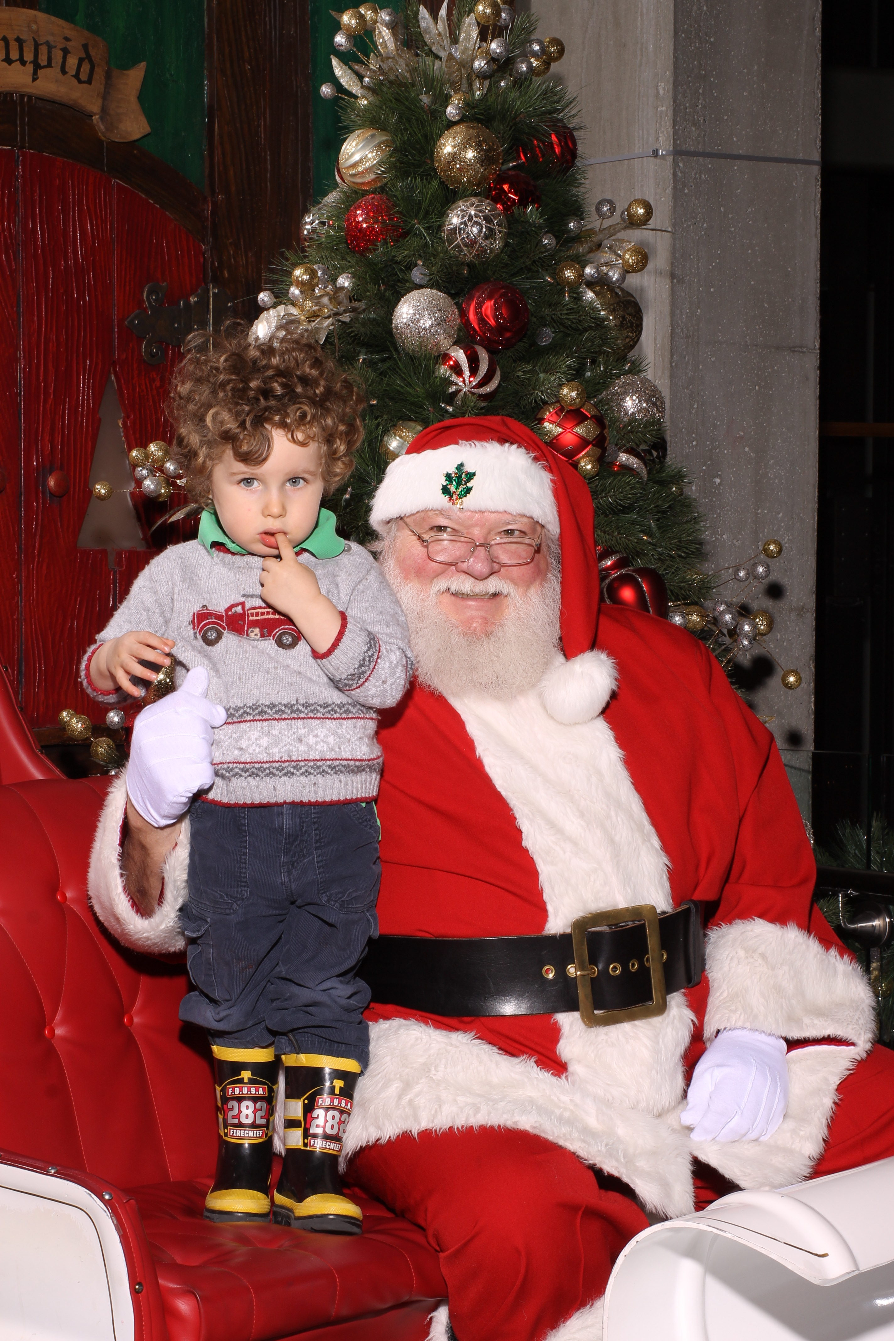 A two year old child looks slightly scared next to Santa's lap.