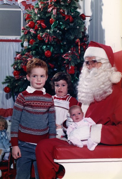 Three young children sit on Santa's lap. 