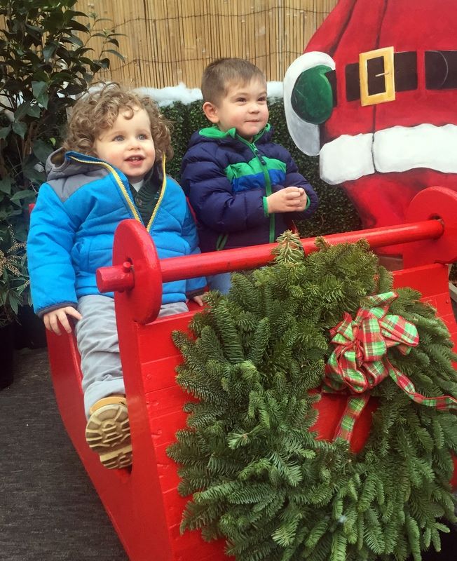 Two toddler boys sit on a santa sleigh and smile at the camera.